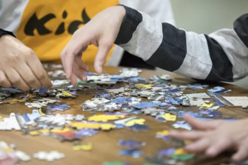 A close-up of two people's hands working on a puzzle. There are puzzle pieces on the table.