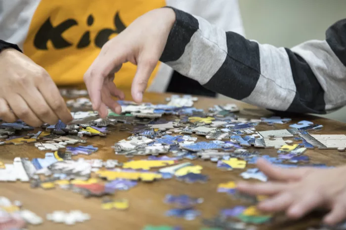 A close-up of two people's hands working on a puzzle. There are puzzle pieces on the table.