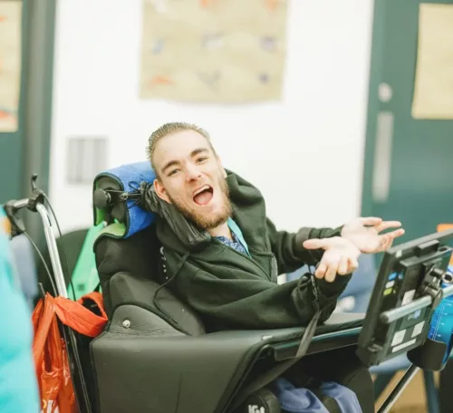 A young man in an electric wheelchair smiling at the camera