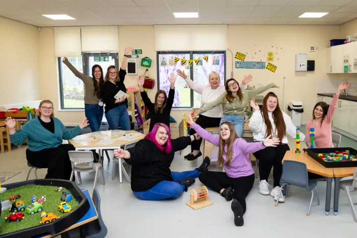 A group of adults in a bright room wave at the camera