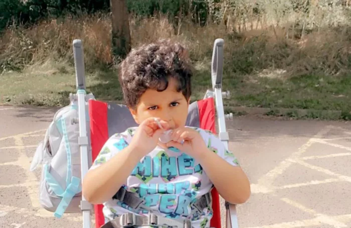 Arsh is sitting in his buggy. He is wearing black trousers and a patterned t-shirt.