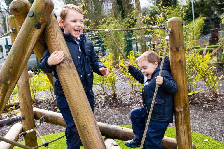Two young boys play on an outdoors climbing frame