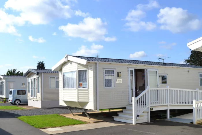 A static caravan in a caravan site. There are steps up to an open door and a bay window with a Kids poster in it.