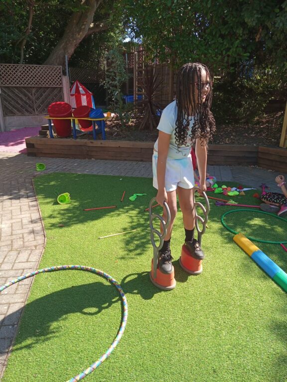 A child is playing outdoors with circus items. The child is standing on individual feet pedestals with handles.