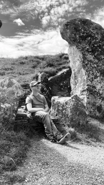 Nathan is oudtoors, sitting on a rock formation. The image is in black and white.