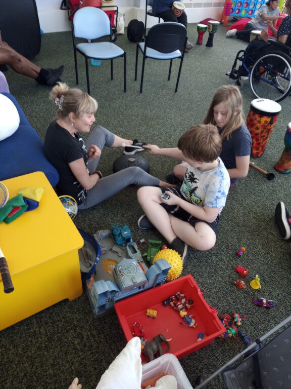 A staff member is playing on the floor with two children. There are toys on the floor.