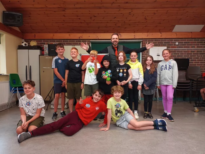 Young carers are taking a group photo with a magician, who is standing behind them with his arms stretched out.