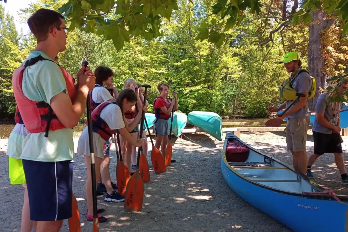 A group of young people and an instructor stand in front of a canoe