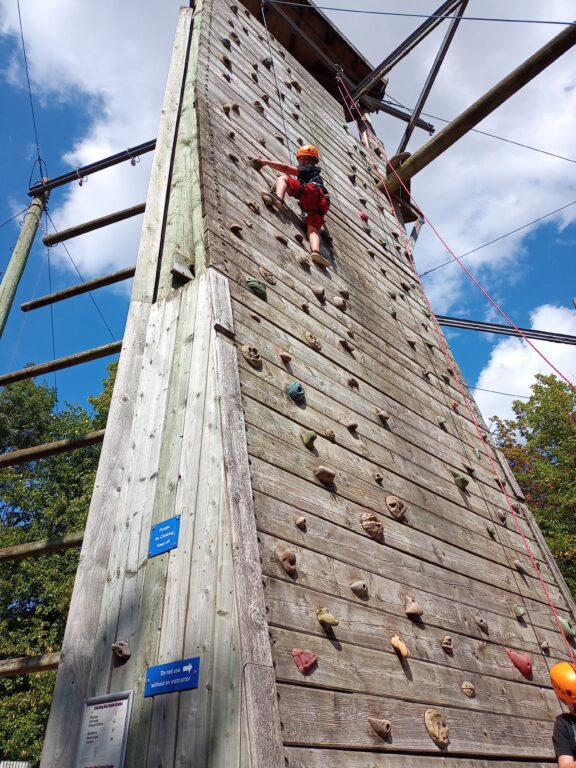 A young carer is climbing up an outdoors climbing wall. 