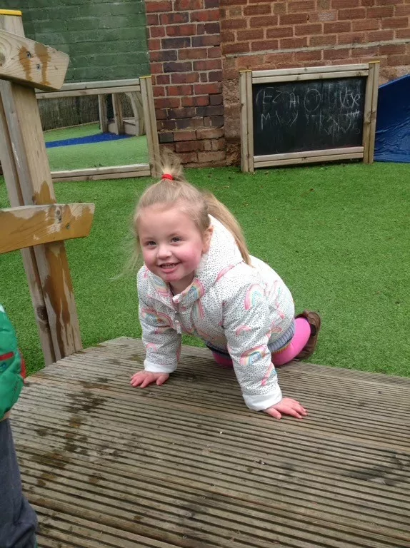 Ivy is crawling over a wooden bridge. She is wearing a puffy white coat and pink tights.