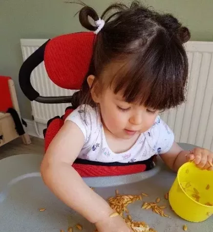 Jessica is sitting on a high chair. She has short brown hair and a thick fringe.