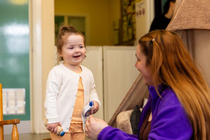 child smiling and playing with Kids staff member in nursery