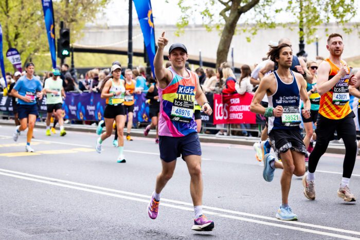 man wearing a kids branded vest waving and smiling running the london marathon
