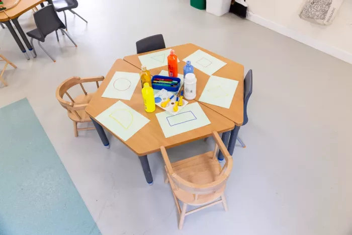 A small set of table and chairs for toddlers to sit on. There are sheets of paper and other items on the table.