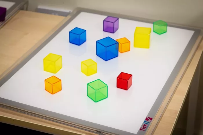 There is a white board placed on a table. On the whiteboard there are orange, green, yellow, blue and purple cubes.