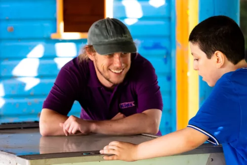 A young boy and a man in a Kids staff t-shirt are talking together and smiling