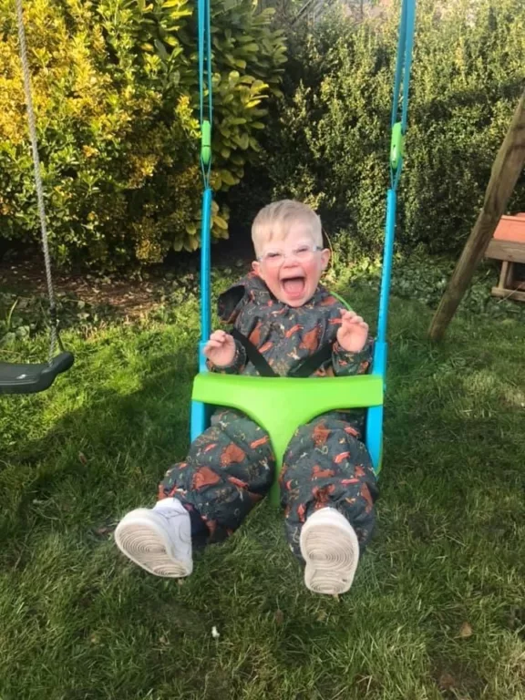 Reuben is on a swing, laughing with his hands stretched out.