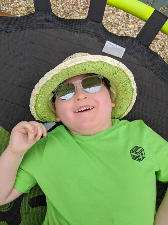 Reuben is lying on a trampoline. He is wearing a lime green t-shirt and a matching hat.