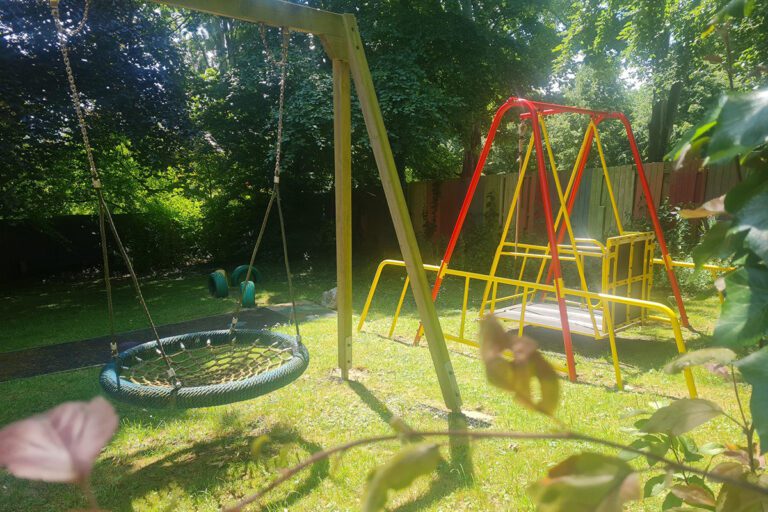 A sunny garden with grass, trees, and various swings suitable for different needs.
