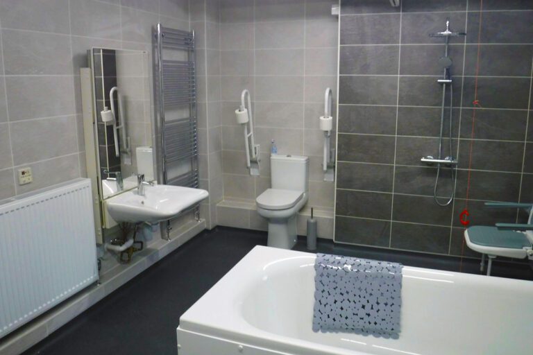 A wet room with a bath, toilet, sink, shower with seat, and radiators.