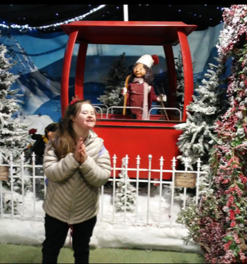Taylor is standing in front of a Christmas prop. She is wearing a coat and black trousers.