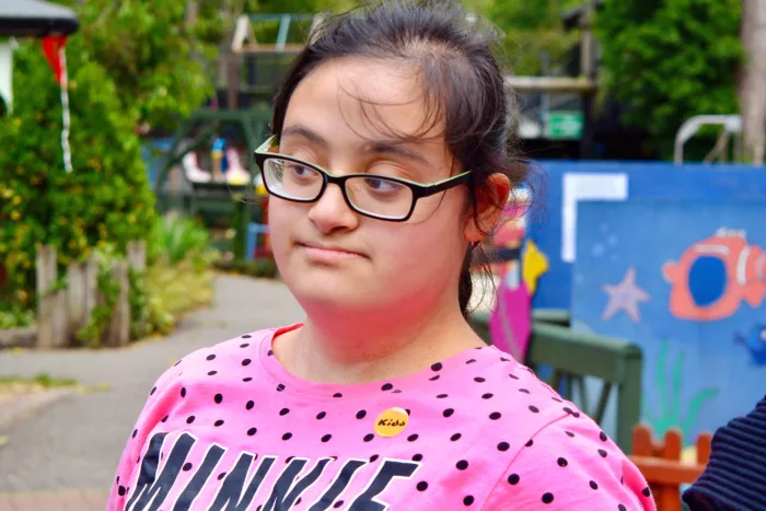 A young person wearing a Minnie t-shirt is standing outside, looking at someone on her right.