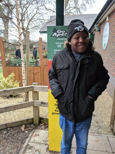 Dan is standing outside at Go Ape. He is wearing a winter coat, jeans and a beanie.