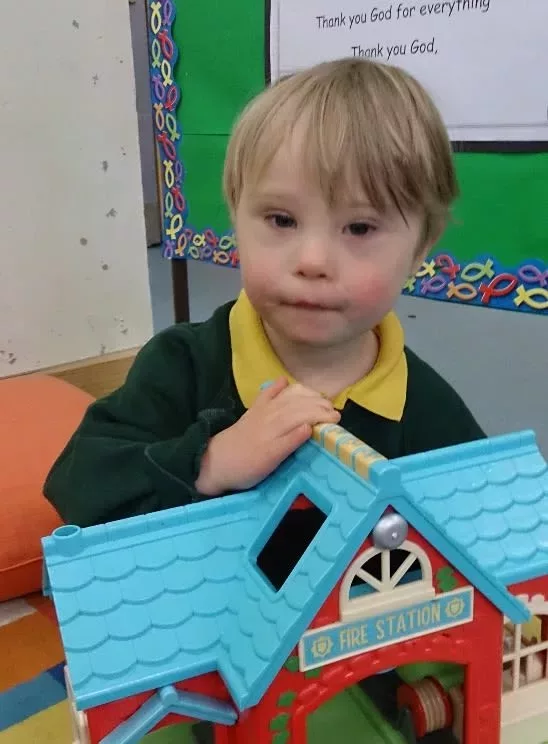 Ollie is holding a playhouse. He is wearing a green and yellow polo.