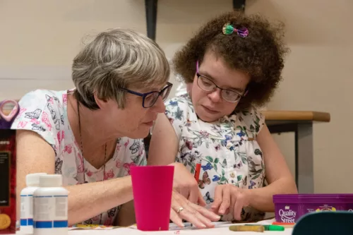 A staff member and young person are sitting together, drawing something on a piece of paper.