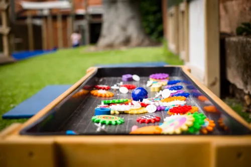 A photo zoomed in on an outdoor play table which contained colourful sensory objects.