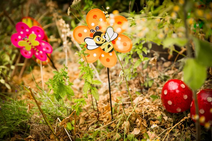 There are two wind spinners sitting in the lawn. They are shaped like flowers and are decorated with a bee and a butterfly.