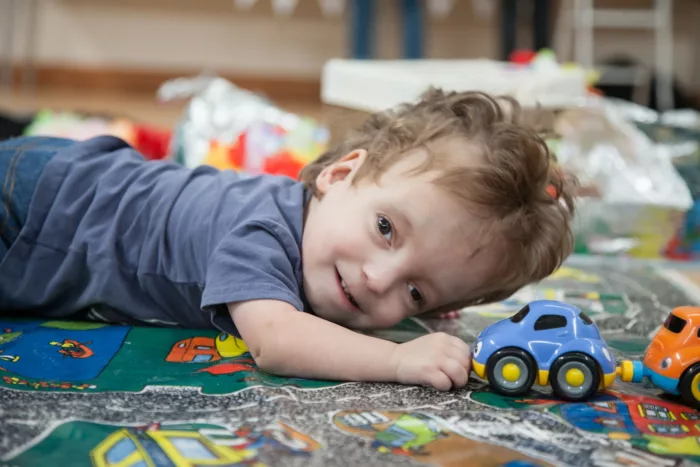 A small boy lies smiling on the ground with a toy car