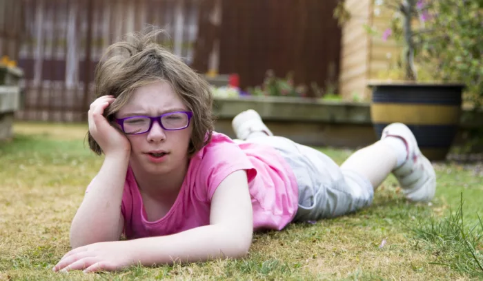 A girl in a pink top and glasses lies outside on the grass