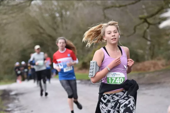 A woman is running the Birmingham Half. Behind her there are blurred out people who are also running.