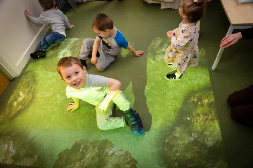 Children are sitting on the floor. Lights are projected on the ground for them to look at.