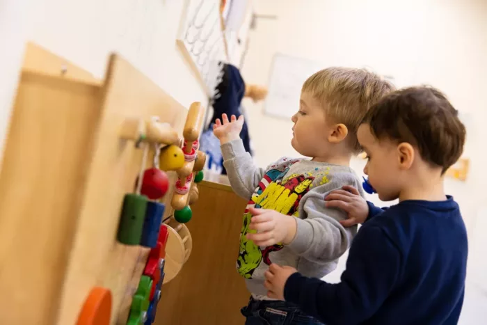 Two boys are playing with toys attached to a board on the wall.