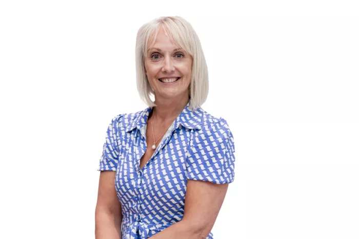 Helen is photographed against a white background. She is wearing a blue and white checkered shirt.