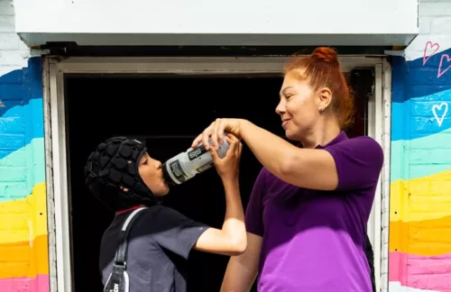 A staff member is helping a child drink water from a water bottle.