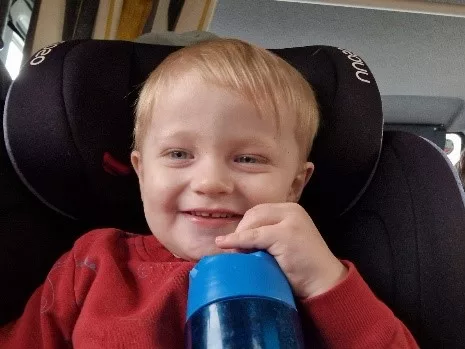 Jenson is sitting on a car seat and is holding a blue water bottle.