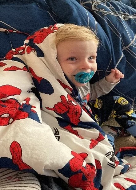 Jenson is wrapped in a Spiderman blanket. He has a pacifier in his mouth.