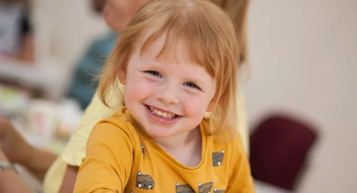 A young girl in a bright top smiles and looks happy