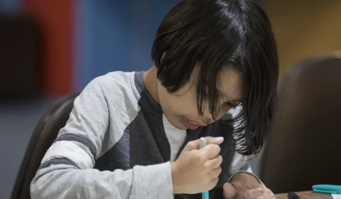 A boy sits at a table drawing.