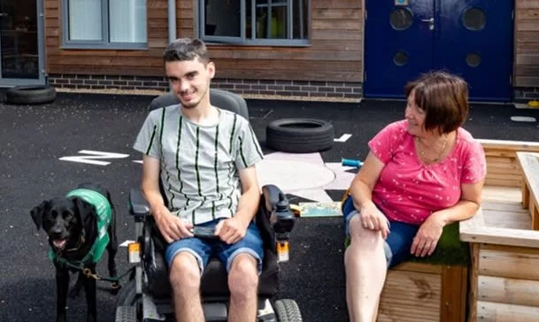 A young man in a wheelchair and an older woman sit together smiling