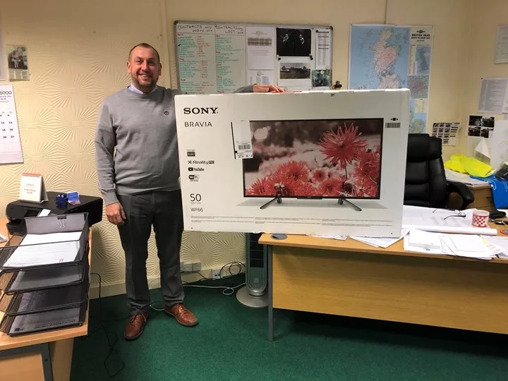 Andy is in an office, one hand on a big box containing a new TV for Kids.