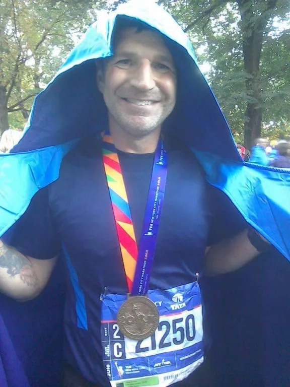 Richard is wearing a poncho over his sports clothes. He is wearing a London Marathon medal.