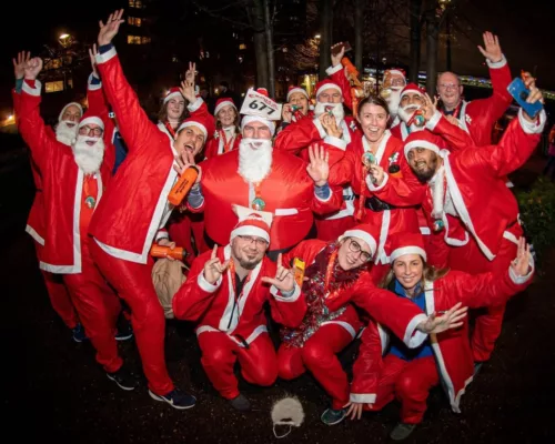 A group of runners wearing Santa costumes are cheering outside. They are wearing medals.