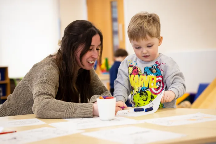 A woman and a child are sitting around a table, looking at a piece of paper