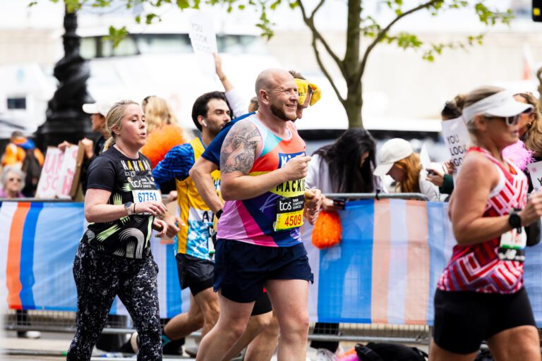 A man is running. He is wearing a Kids vest and has a tattoo on his right arm