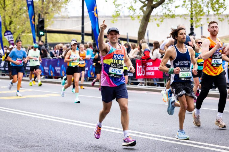 A man in a Kids vest is running with one hand up