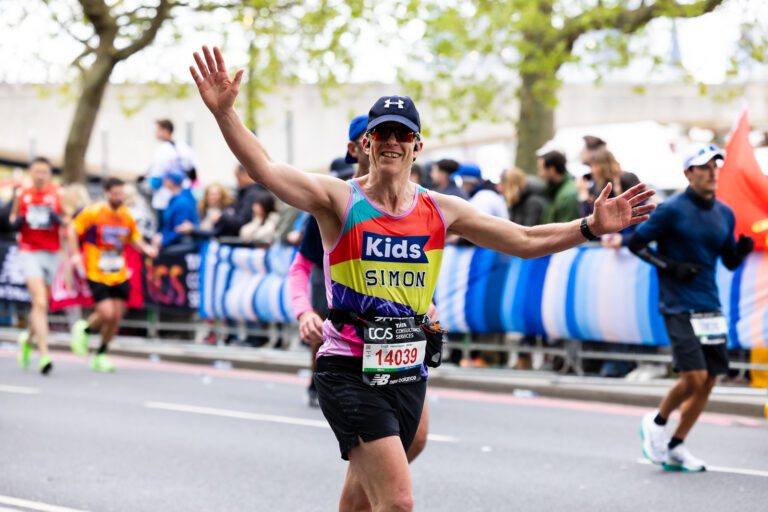 A runner in a Kids vest is running with his hands up in the air